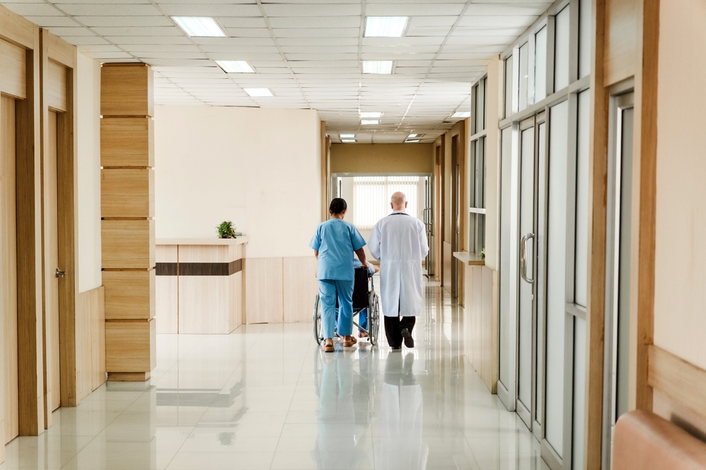 Two,Healthcare,Professionals,Escort,A,Patient,In,A,Wheelchair,Down